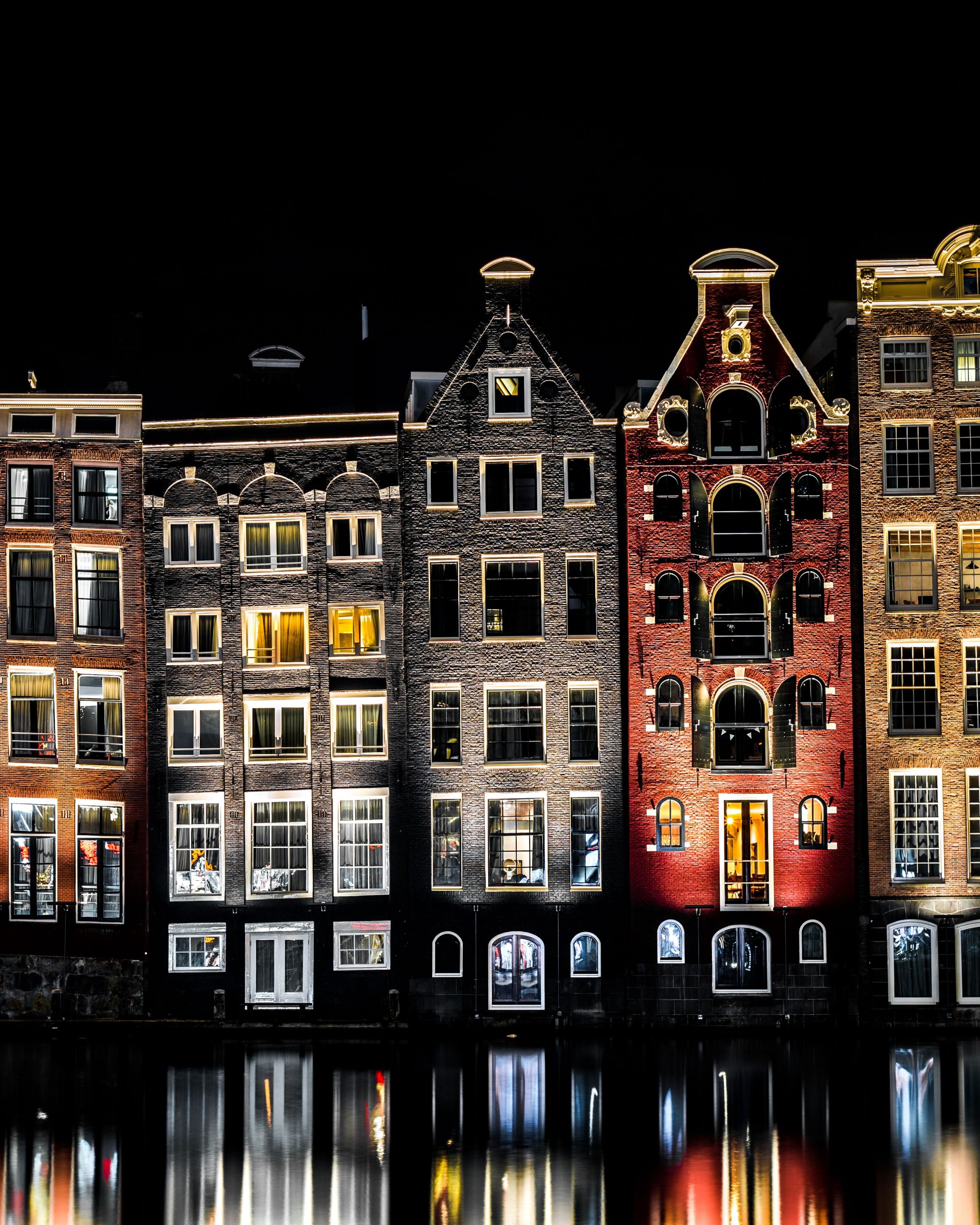 Illuminated canal houses of Amsterdam at night reflecting on the water, showcasing traditional Dutch architecture