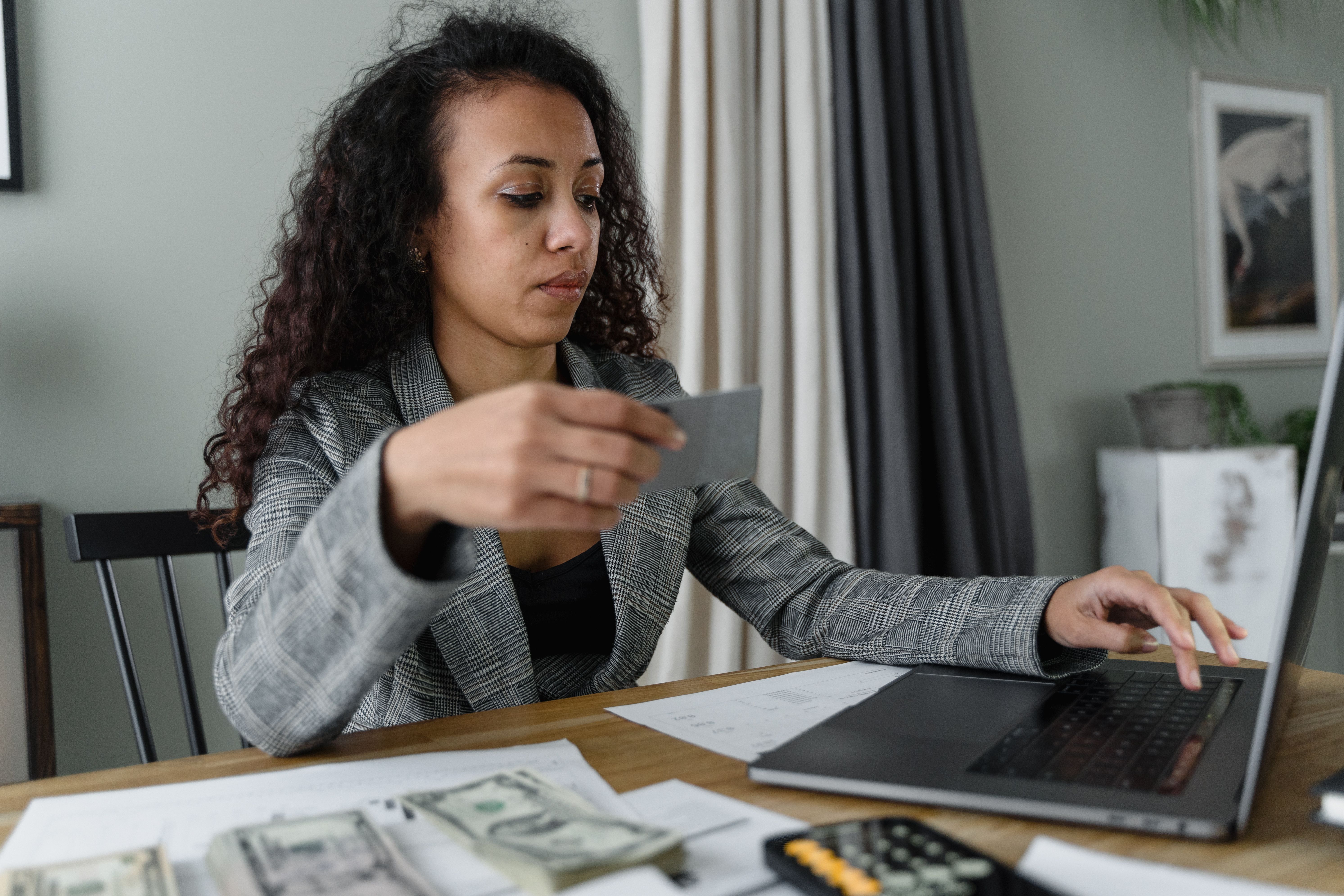 Digital entrepreneur using a laptop while managing cash and a payment card, illustrating income and expense management.