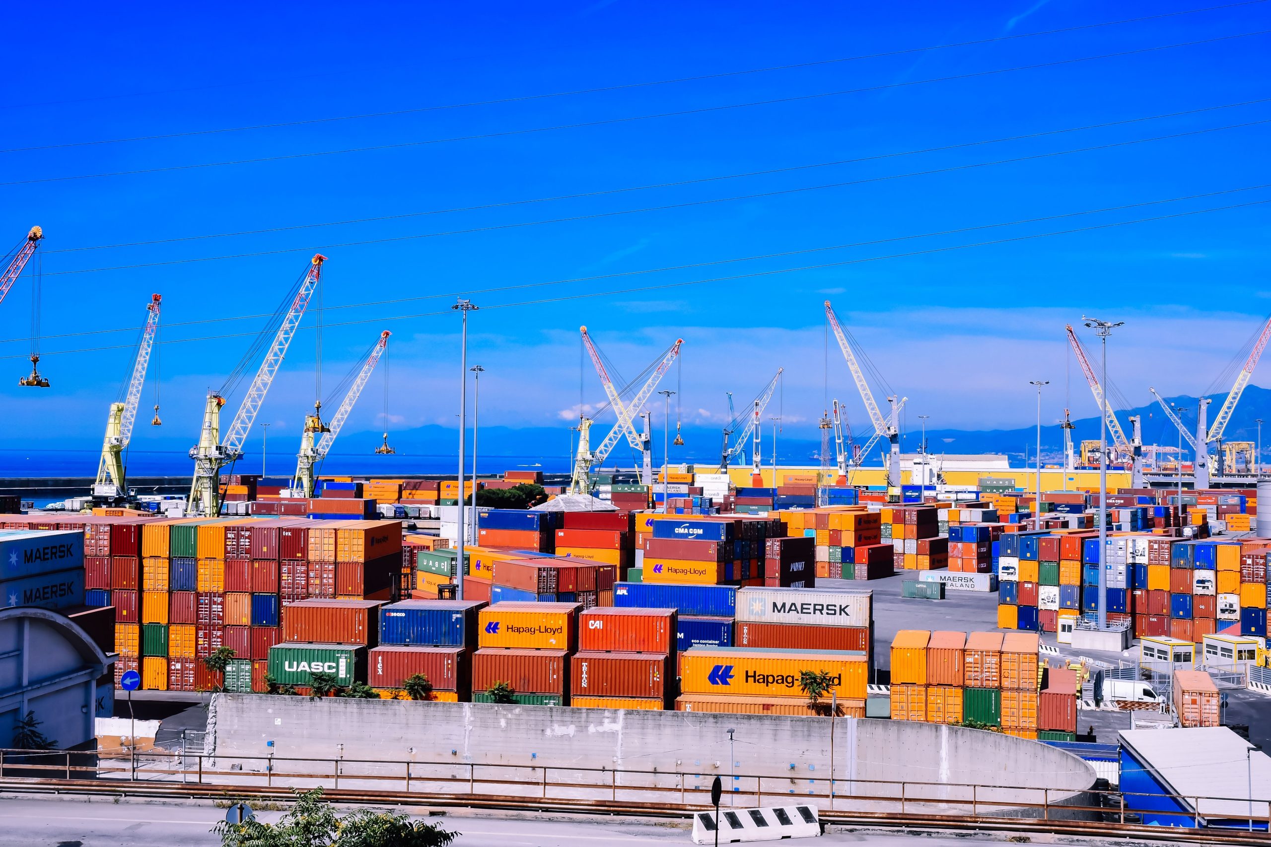 Bustling shipping port with stacked cargo containers and cranes, illustrating global supply chain disruption.