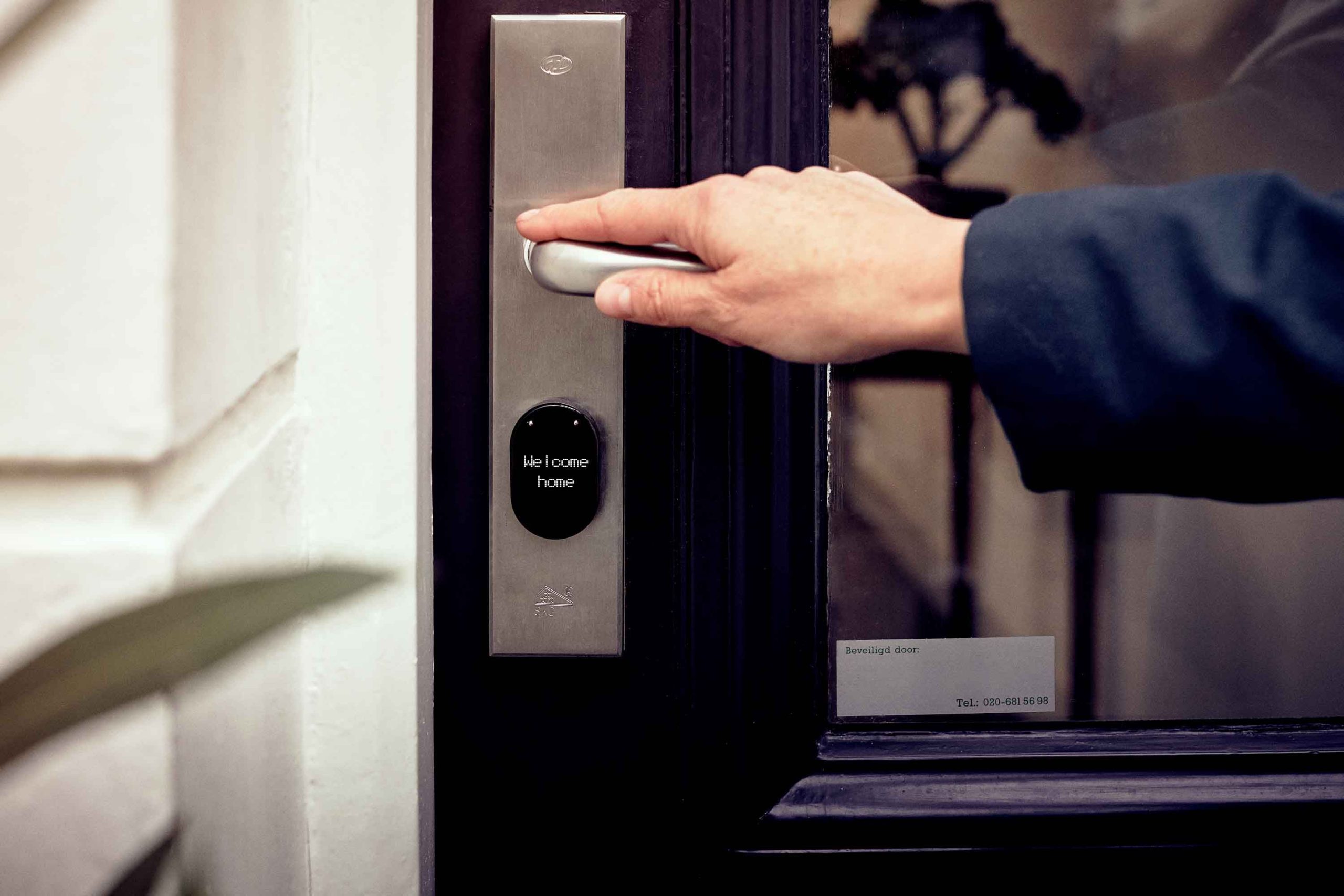 Hand opening a smart home door with a digital access panel, illustrating controlled entry security.