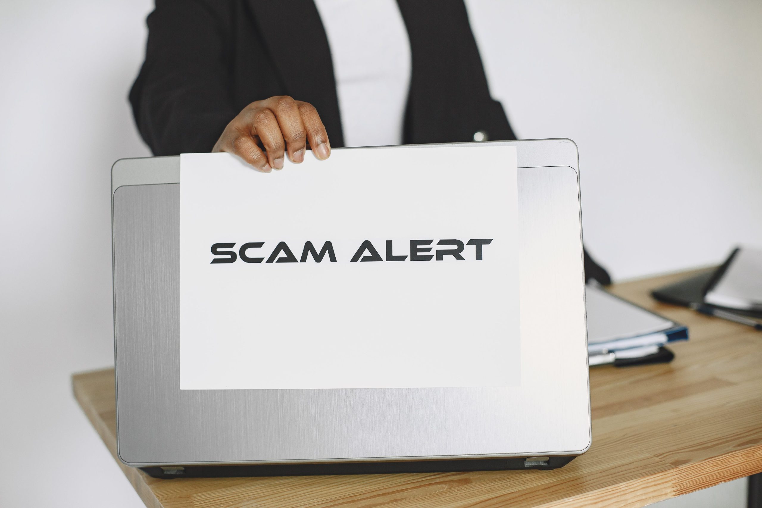 Business person holding a scam alert sign over a laptop, illustrating warnings about fraudulent Telegram accounts and impersonation.